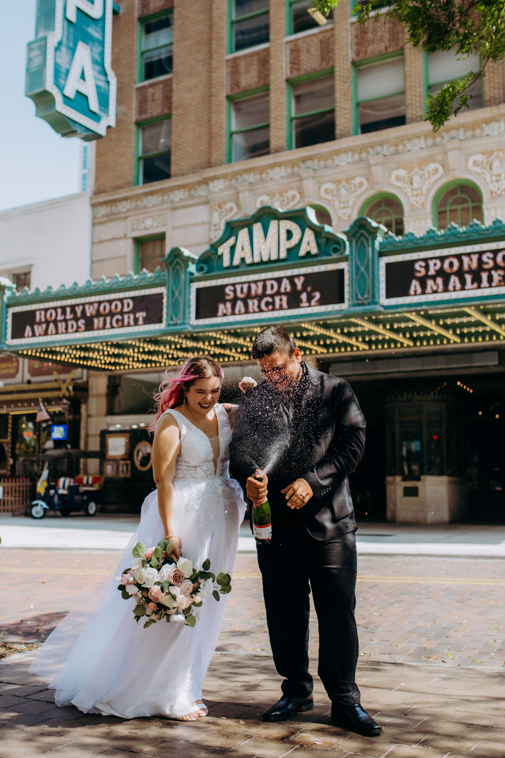 couple popping champagne in the middle of the street in downtown tampa in front of the tampa theatre celebrating eloping