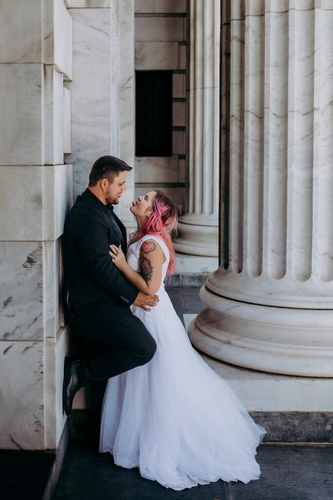 grom is leaning against the wall of the courthouse as bride leans in to him and playfully sticks out her tongue at him after their tampa courthouse weeding 