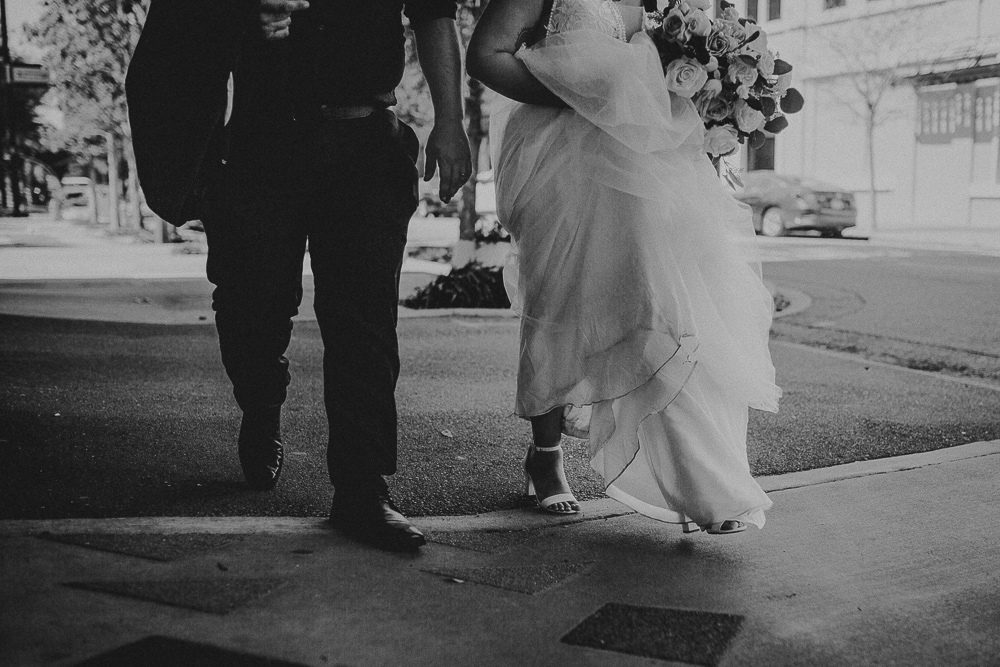 picture of the bride holding her dress and the groom holding his jacket as they walk down the street downtown just married