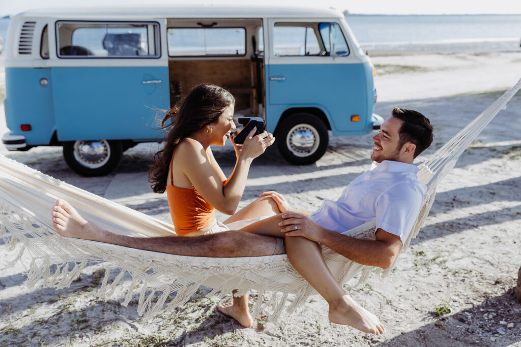 couple taking photos of one another in a hammock on the beach with a polaroid camera for elopement in tampa