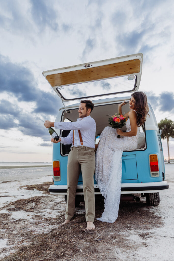 couple popping champagne on the beavh after their elopement in tampa florida