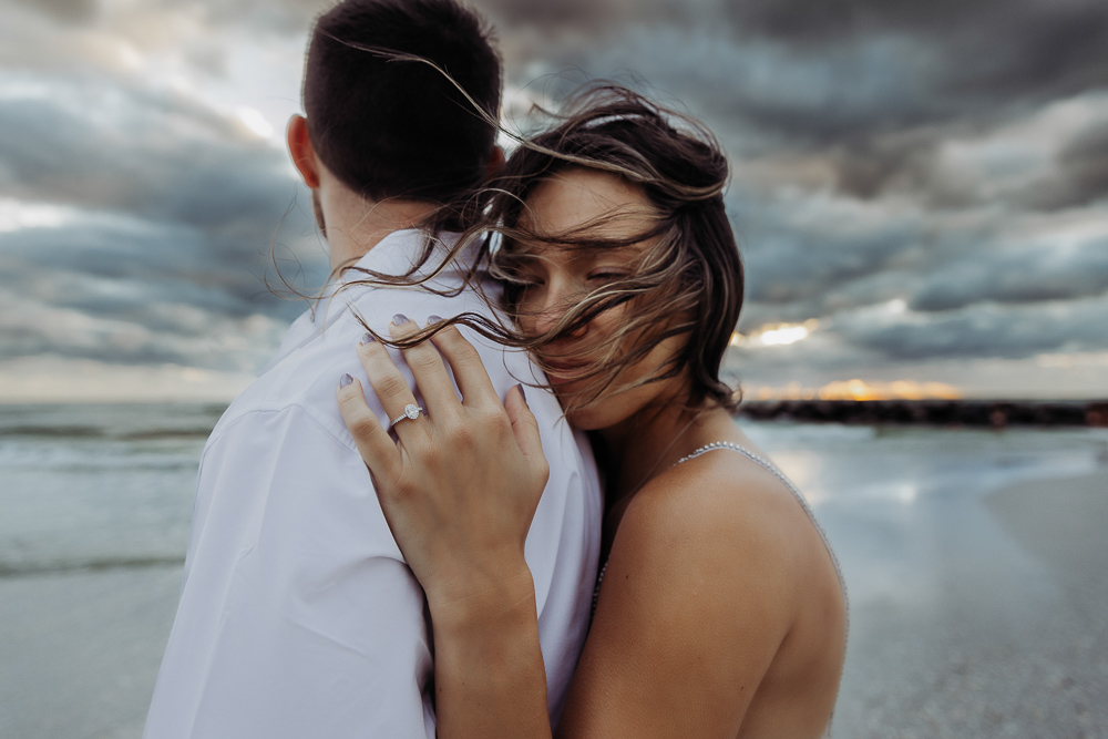 future bride hugging her husband during sunset on st pete beach during their engagement session with tampa wedding photographer