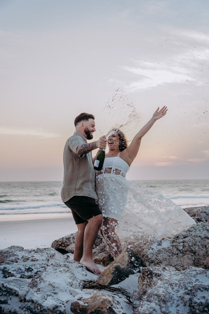 couple popping champagne at sunset on the beach during their florida elopement in st pete