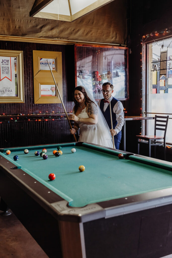 couple laughing and being silly while playing pool after their elopement 